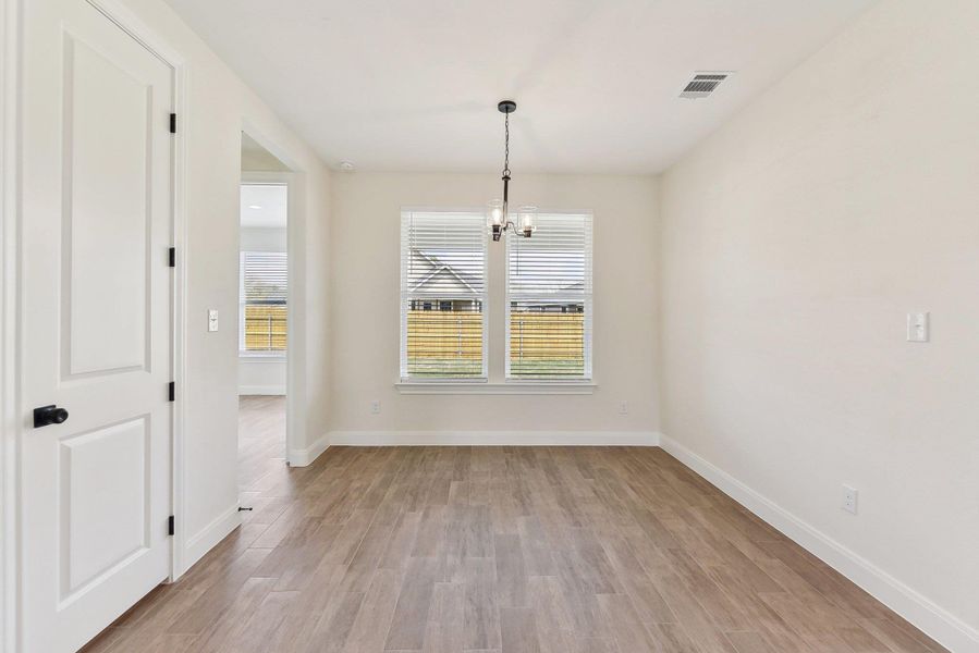 Unfurnished dining area featuring light wood-type flooring, baseboards, a notable chandelier, and visible vents Unfurnished dining area featuring light wood-type flooring, baseboards, a notable chandelier, and visible vents