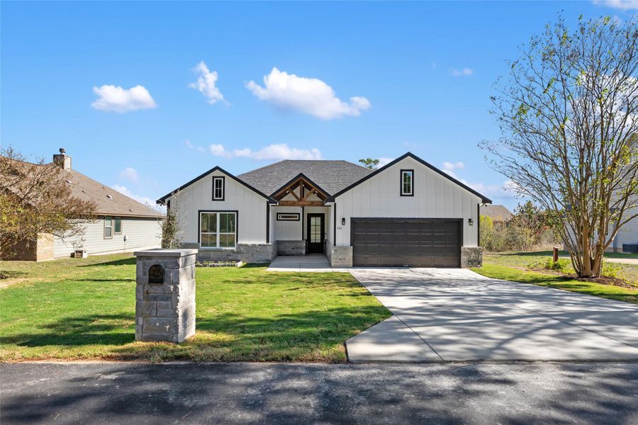 Modern farmhouse style home featuring board and batten siding, a front yard, concrete driveway, and stone siding
