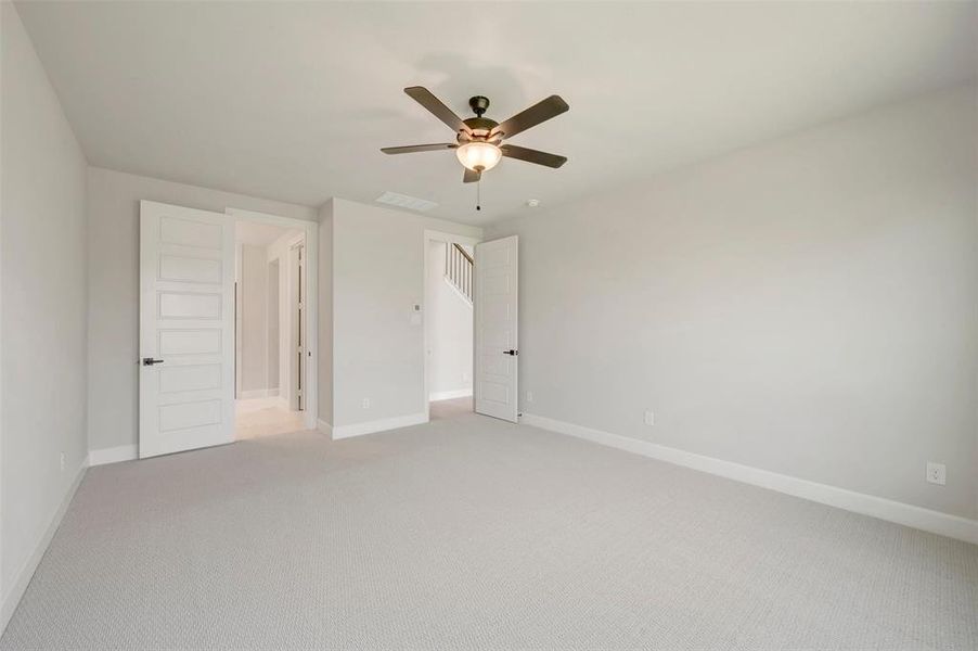 Spacious room featuring light gray walls, plush gray carpeting, a dark wood-finish ceiling fan with integrated lighting, and white five-panel interior doors