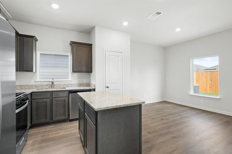 Kitchen with a kitchen island, appliances with stainless steel finishes, light wood-style flooring, light stone counters, and recessed lighting