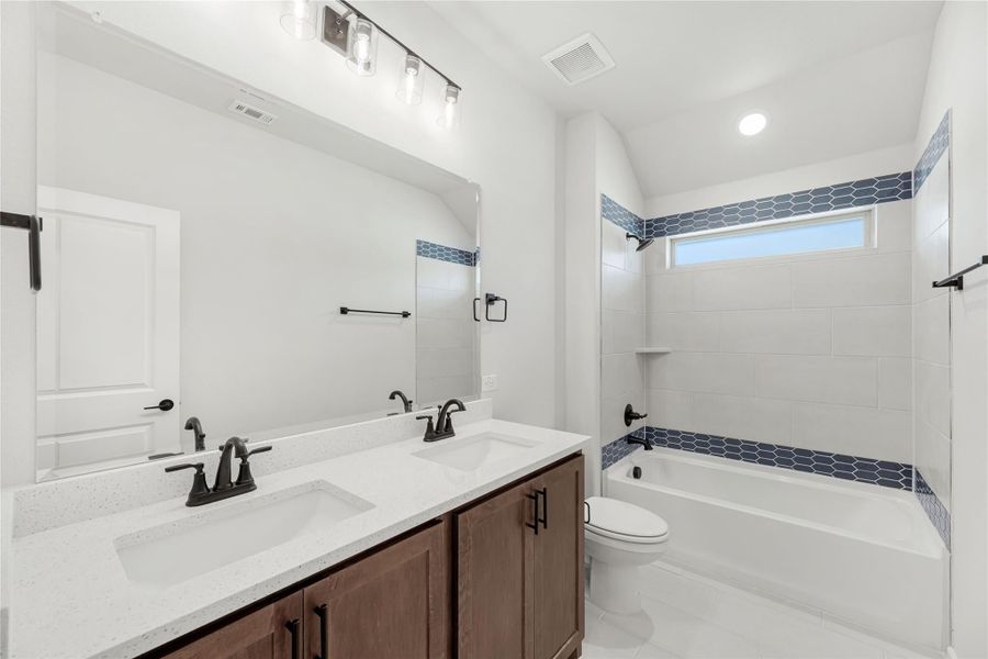 Bathroom with double sink vanity, quartz countertop, and tiled tub surround with blue accent tiles Bathroom with double sink vanity, quartz countertop, and tiled tub surround with blue accent tiles