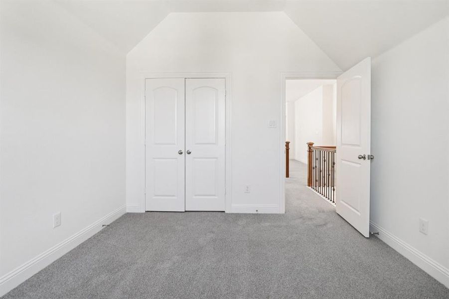 Unfurnished bedroom with carpet flooring, vaulted ceiling, and a closet Unfurnished bedroom with carpet flooring, vaulted ceiling, and a closet