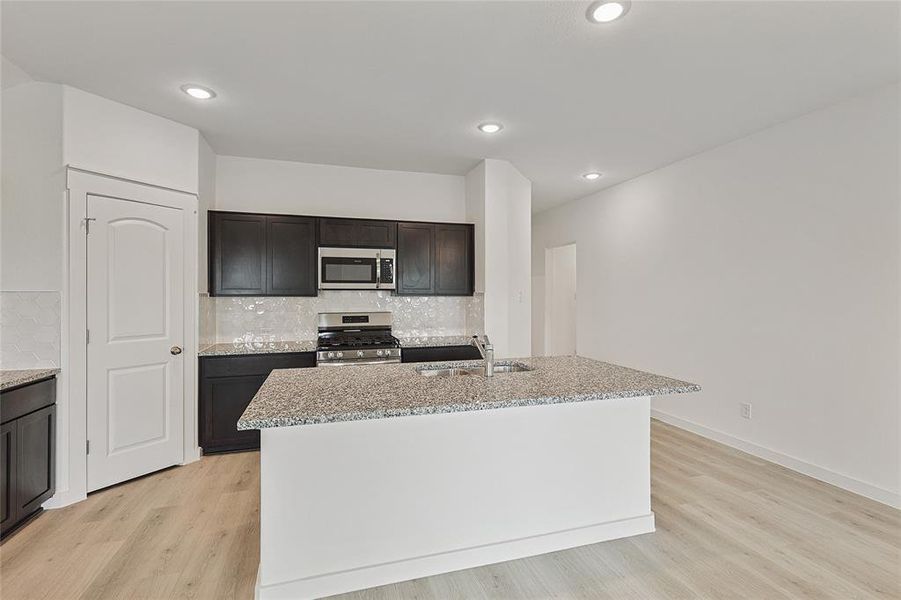 Kitchen featuring decorative backsplash, an island with sink, stainless steel appliances, and light wood-type flooring