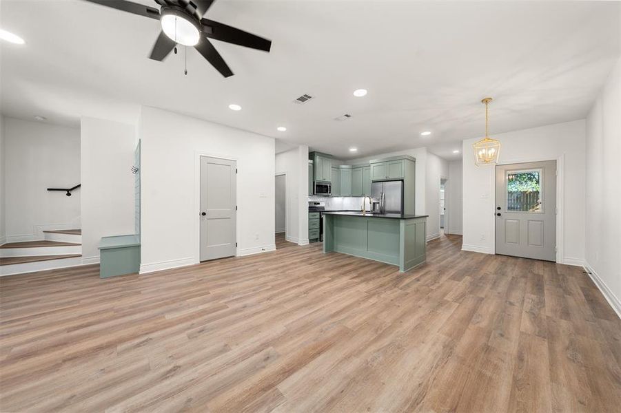 Unfurnished living room with recessed lighting, light wood-style flooring, a ceiling fan, and stairs Unfurnished living room with recessed lighting, light wood-style flooring, a ceiling fan, and stairs
