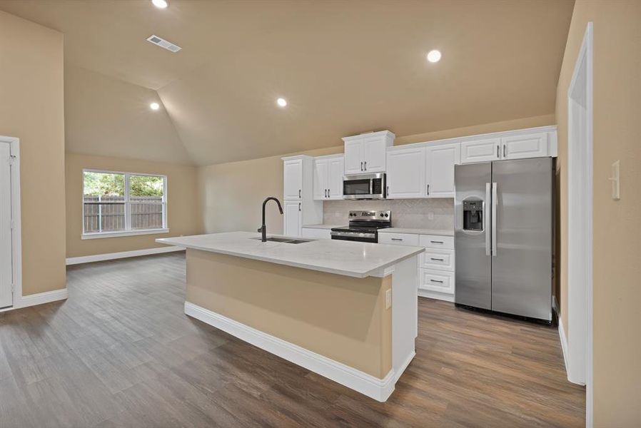 Kitchen featuring lofted ceiling, visible vents, a sink, a center island with sink, and appliances with stainless steel finishes Kitchen featuring lofted ceiling, visible vents, a sink, a center island with sink, and appliances with stainless steel finishes
