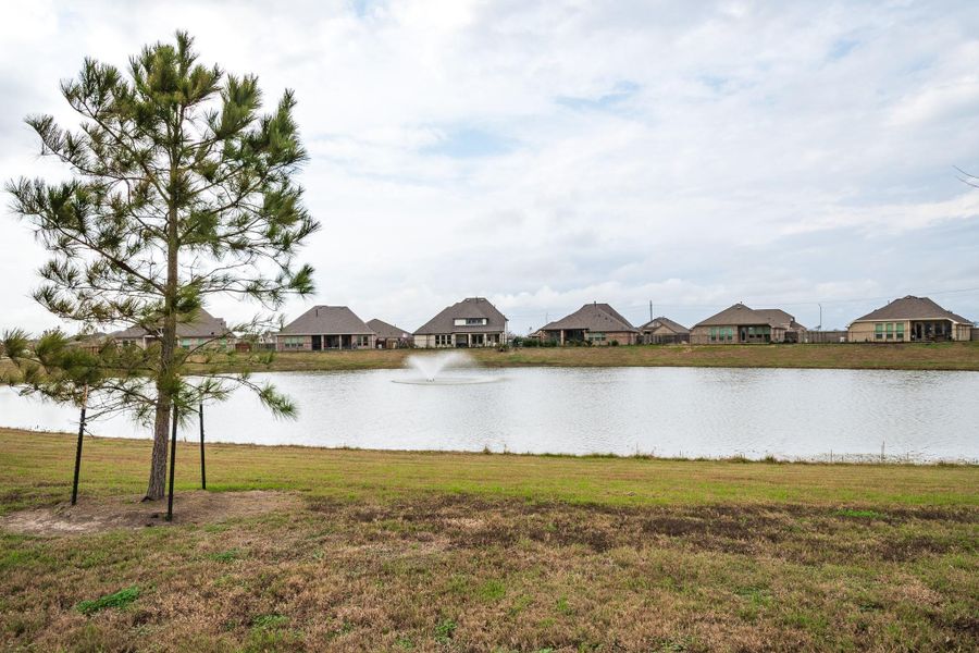 A view of a serene neighborhood lake with a fountain, flanked by modern homes and a tree in the foreground, offering peaceful waterfront living. A view of a serene neighborhood lake with a fountain, flanked by modern homes and a tree in the foreground, offering peaceful waterfront living.