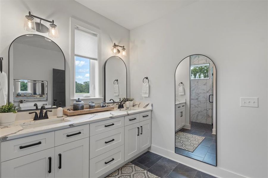 Spa-inspired primary bath featuring dual vanities, designer lighting, sleek black hardware, and a spacious walk-in shower with refined tilework—creating a polished, luxury retreat with modern country elegance.