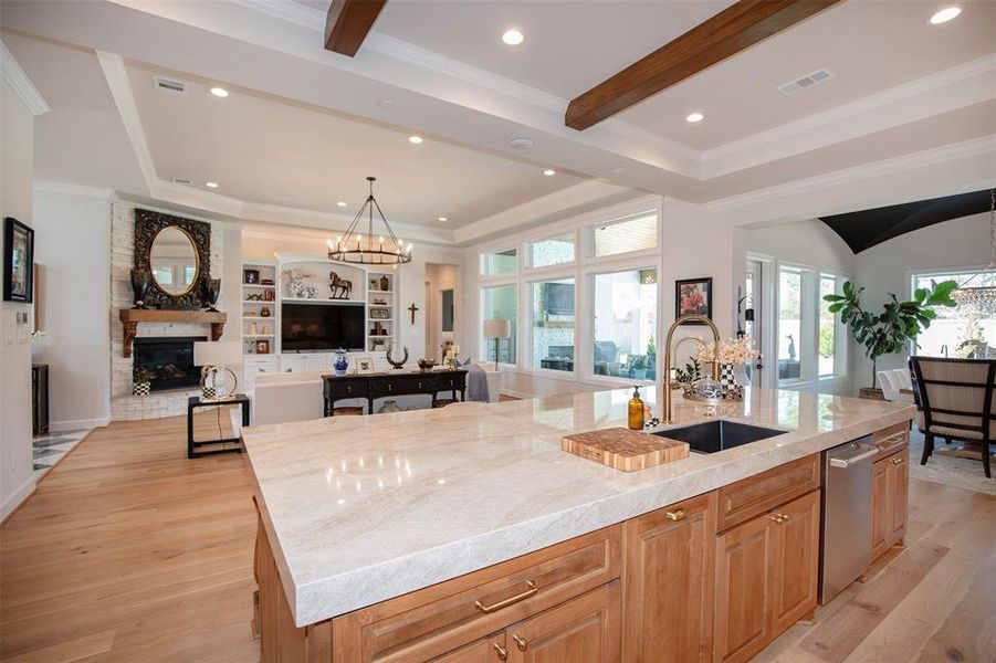 This photo showcases a spacious open-concept living area with a modern kitchen featuring a large island and sink. The room is bright with natural light from large windows, elegant wood floors, and a cozy fireplace. It's perfect for entertaining and family gatherings.