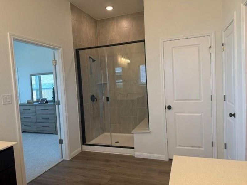 Spacious walk-in shower with floor-to-ceiling tile surround, built-in bench, and clear glass enclosure with matte black trim