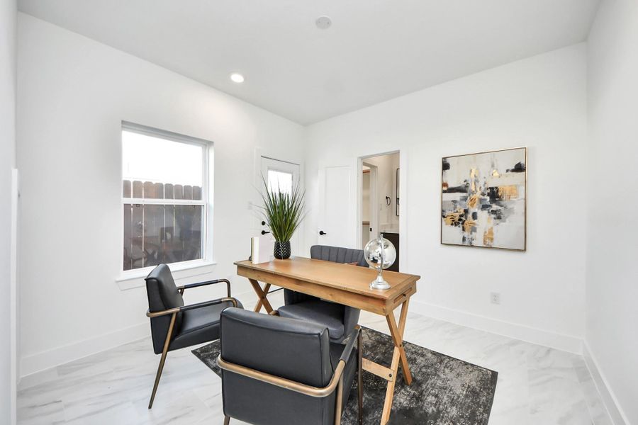This photo showcases a bright, modern home office with white walls, a large window, and sleek furnishings. The space features a wooden desk, black chairs, and abstract artwork, creating a clean, inviting work environment.