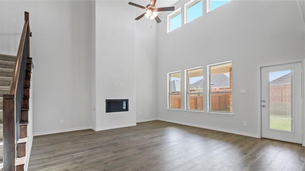 Unfurnished living room with stairs, a glass covered fireplace, dark wood-type flooring, a high ceiling, and a ceiling fan