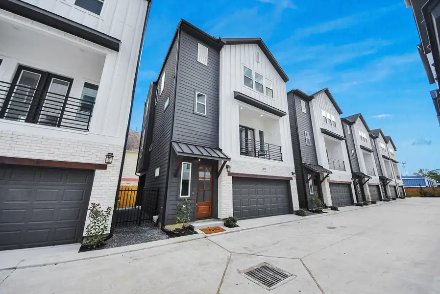 This modern townhouse welcomes you with a sleek exterior in white and dark gray siding, a warm wooden door, a two-car garage, and a balcony. A small landscaped area enhances curb appeal, making it perfect for contemporary living. This modern townhouse welcomes you with a sleek exterior in white and dark gray siding, a warm wooden door, a two-car garage, and a balcony. A small landscaped area enhances curb appeal, making it perfect for contemporary living.