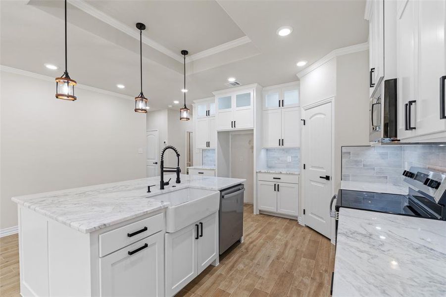 Kitchen featuring hanging light fixtures, an island with sink, appliances with stainless steel finishes, light hardwood / wood-style floors, and white cabinetry