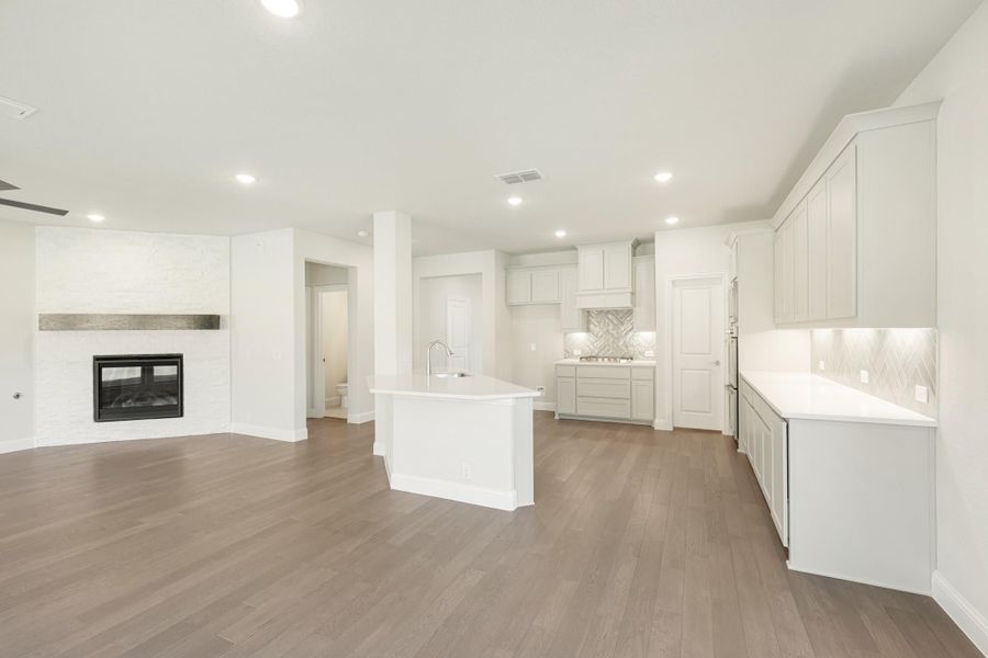 Open-concept kitchen and living area with white cabinets, center island, tile backsplash, and fireplace on wood floors.
