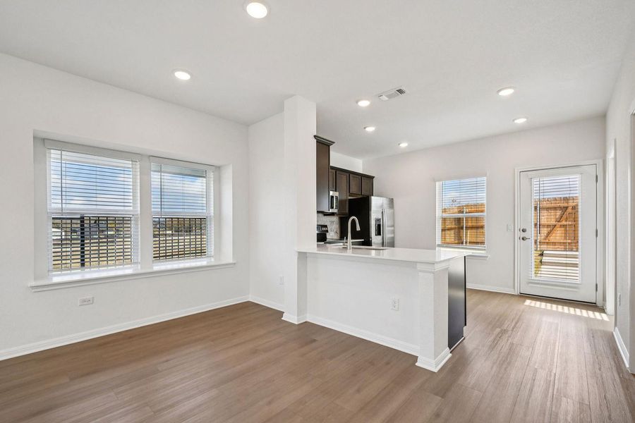 Kitchen featuring dark wood-type flooring, dark brown cabinets, stainless steel fridge, a peninsula, and recessed lighting