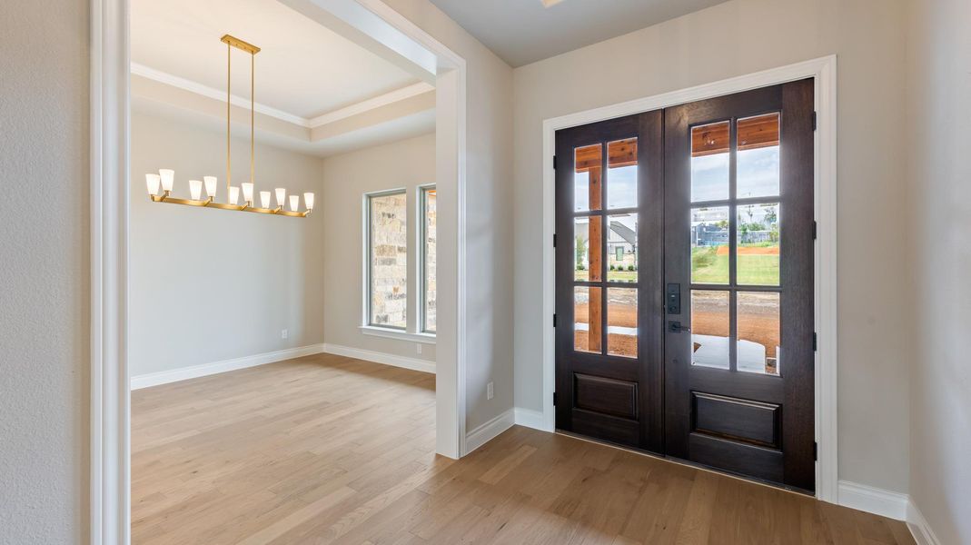 Doorway featuring wood finished floors, french doors, ornamental molding, a raised ceiling, and a chandelier