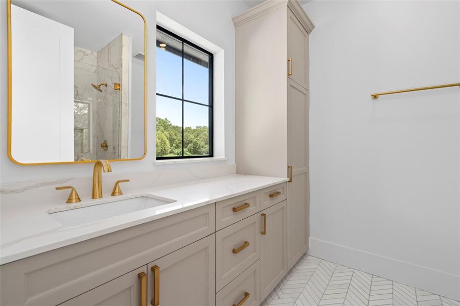 Designer vanity with quartz countertops, custom cabinetry, brushed gold fixtures, and a striking herringbone tile floor. Designer vanity with quartz countertops, custom cabinetry, brushed gold fixtures, and a striking herringbone tile floor.