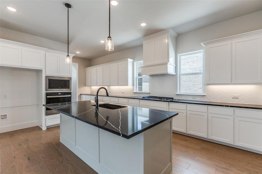 Kitchen with white cabinets, stainless steel appliances, sink, hardwood / wood-style flooring, and a center island with sink