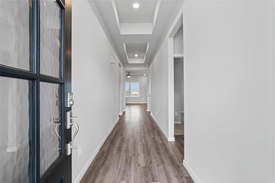 This entryway features a modern, open-concept design. The long, bright corridor utilizes a neutral color palette, recessed lighting, and luxury vinyl flooring to lead the eye toward the home's main living area.