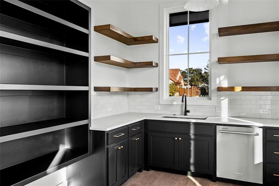 Kitchen featuring dishwasher, dark cabinets, tasteful backsplash, and light stone counters Kitchen featuring dishwasher, dark cabinets, tasteful backsplash, and light stone counters