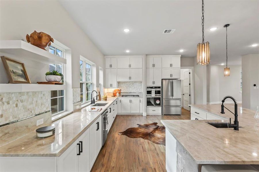 Kitchen with light stone countertops, white cabinets, decorative light fixtures, dark wood-type flooring, and appliances with stainless steel finishes Kitchen with light stone countertops, white cabinets, decorative light fixtures, dark wood-type flooring, and appliances with stainless steel finishes
