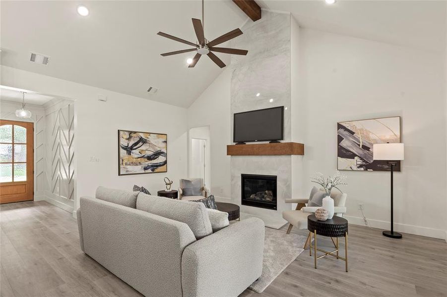 Living room with high vaulted ceiling, wood finished floors, a ceiling fan, a fireplace, and beam ceiling