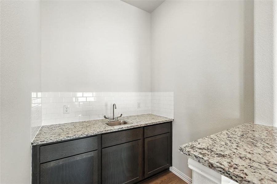 Kitchen with light stone countertops, dark wood finish cabinetry, backsplash, and dark wood finished floors