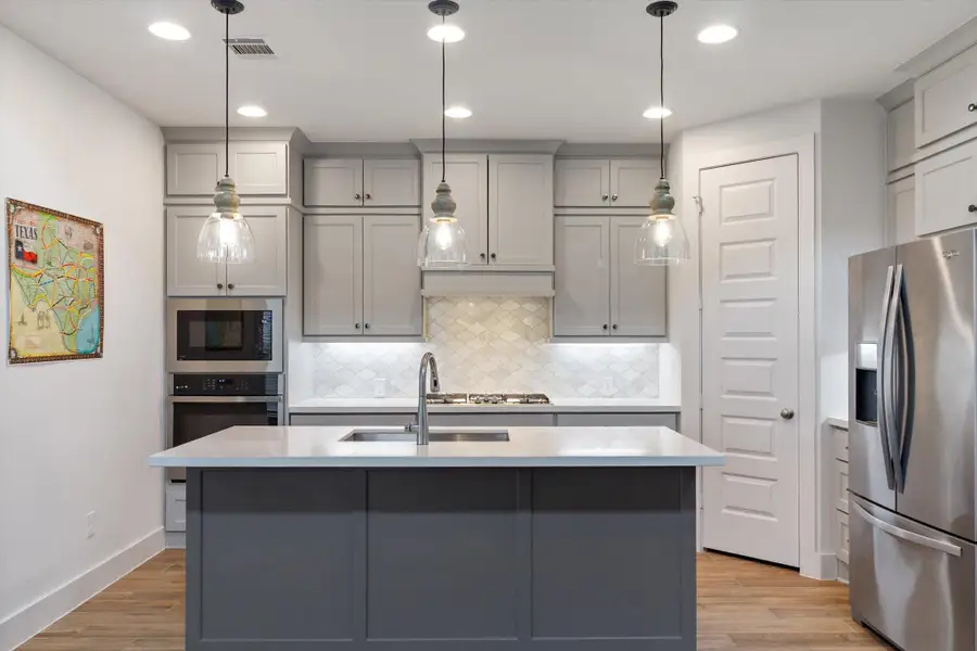 Kitchen featuring gray cabinets, appliances with stainless steel finishes, decorative backsplash, light wood-style flooring, and recessed lighting
