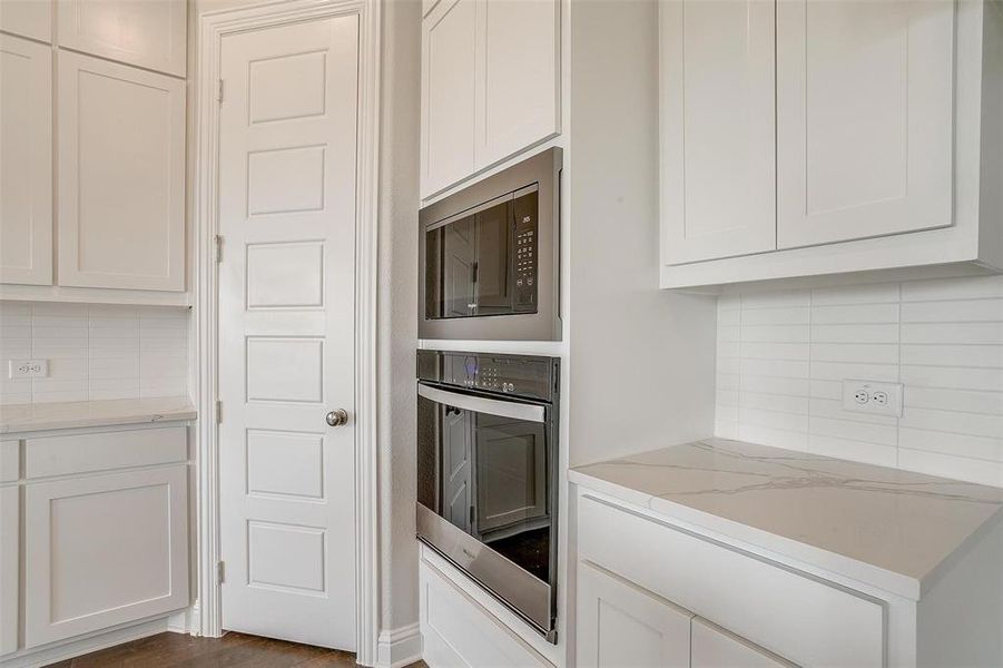 Kitchen featuring stainless steel oven, built in microwave, tasteful backsplash, white cabinetry, and dark hardwood / wood-style flooring