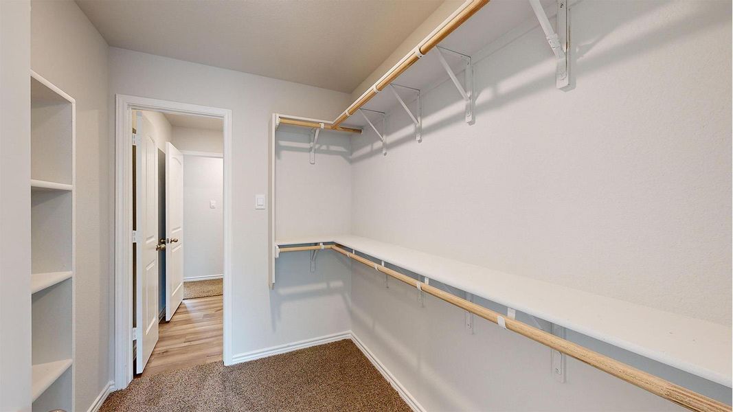 Spacious walk-in closet featuring built-in shelving, two levels of hanging rods, and light-colored carpeting Spacious walk-in closet featuring built-in shelving, two levels of hanging rods, and light-colored carpeting