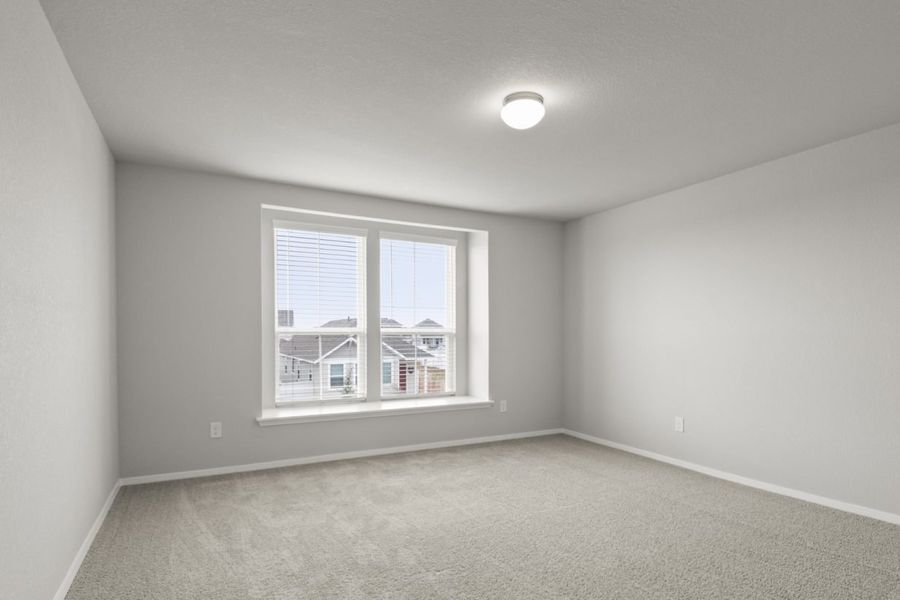 Image of a primary bedroom with tan carpeting and light grey painted walls with two large windows