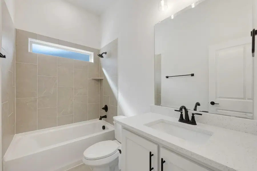 Bathroom with tiled tub-shower combo, white vanity with quartz countertop, and black fixtures