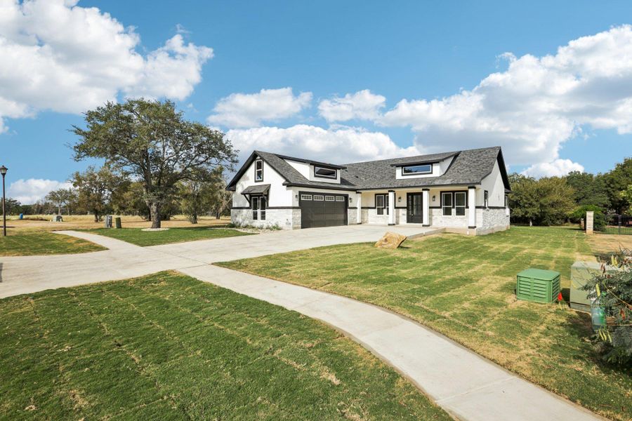Modern farmhouse style home with concrete driveway, a front lawn, a garage, roof with shingles, and brick siding