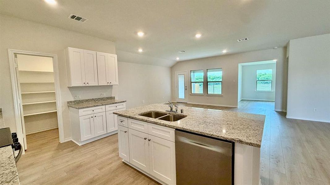 Modern kitchen featuring an expansive center island with an undermount dual sink, white cabinetry, granite-finish countertops, and wood-finish flooring