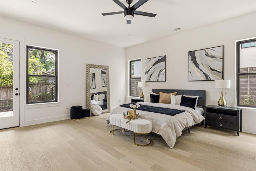 Spacious room featuring light wood-finish flooring, multiple windows with dark frames, a single glass-paneled door, recessed lighting, and a ceiling fan