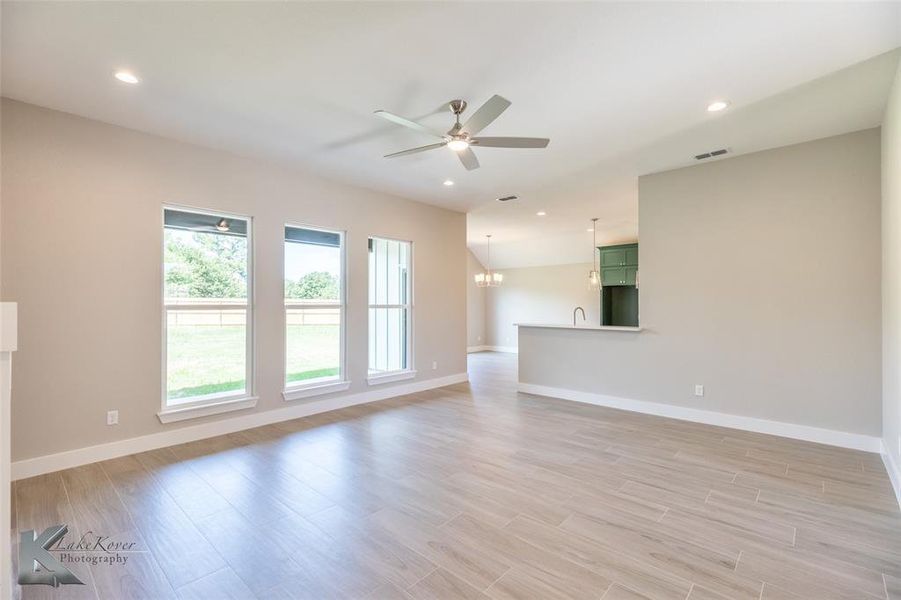 Unfurnished living room featuring ceiling fan, light wood finished floors, a chandelier, and recessed lighting