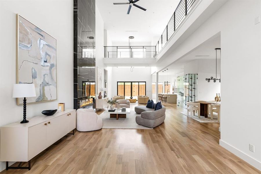 Living area featuring a ceiling fan, light wood-type flooring, a towering ceiling, and a fireplace Living area featuring a ceiling fan, light wood-type flooring, a towering ceiling, and a fireplace