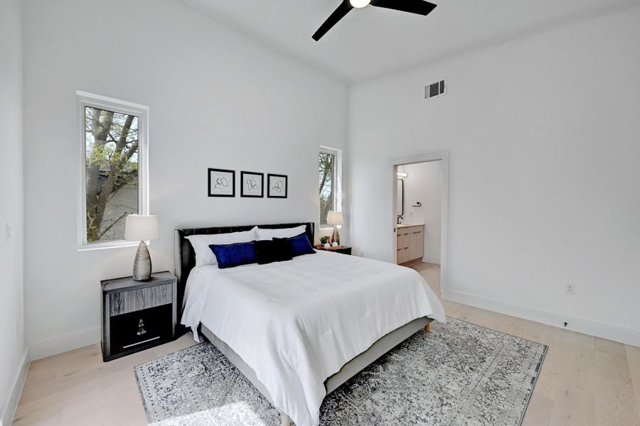 Bedroom with light wood finished floors, visible vents, connected bathroom, baseboards, and a high ceiling