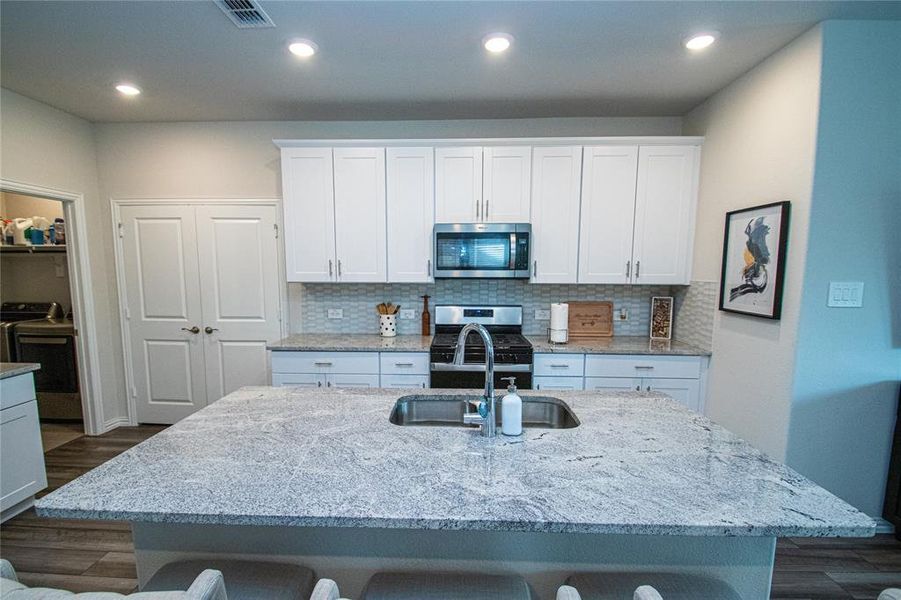 Kitchen featuring light stone countertops, dark wood-style floors, white cabinetry, and recessed lighting Kitchen featuring light stone countertops, dark wood-style floors, white cabinetry, and recessed lighting