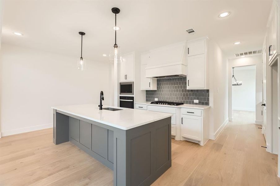 Kitchen featuring stainless steel appliances, light hardwood / wood-style floors, a center island with sink, sink, and white cabinets