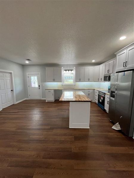 Kitchen with refrigerator, white cabinetry, a textured ceiling, a center island, and stove Kitchen with refrigerator, white cabinetry, a textured ceiling, a center island, and stove