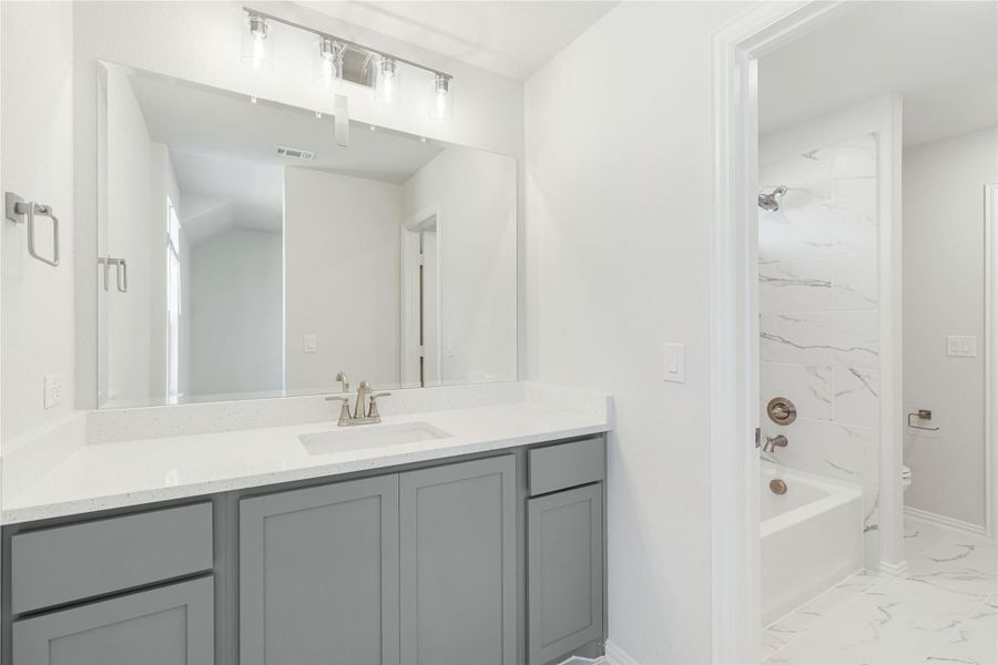 Bathroom with gray vanity, white quartz countertop, large mirror, and marble-tiled tub-shower combo