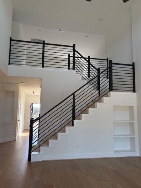 Stairway with built in features, a towering ceiling, baseboards, and wood finished floors