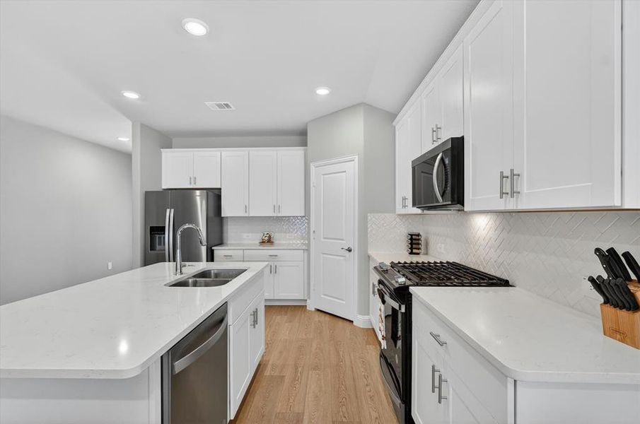 Modern kitchen featuring a large island with an undermount sink, white shaker cabinetry, stainless steel appliances, and wood-finish flooring Modern kitchen featuring a large island with an undermount sink, white shaker cabinetry, stainless steel appliances, and wood-finish flooring