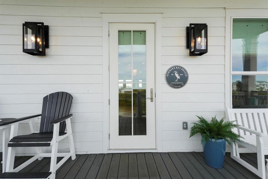 This inviting porch features a central glass door flanked by stylish black lantern lights, offering a cozy seating area with Adirondack chairs to watch the sunrise.