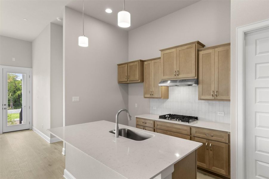 Kitchen with a sink, stainless steel gas cooktop, under cabinet range hood, backsplash, and a high ceiling
