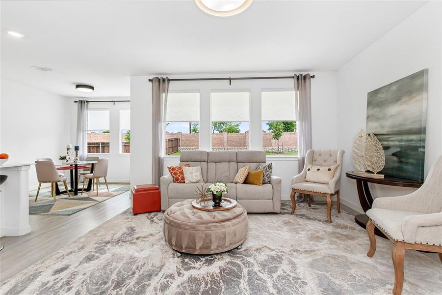 Bright and inviting living space featuring light-colored flooring, windows with blinds and drapes, and an open layout providing a view of the dining area