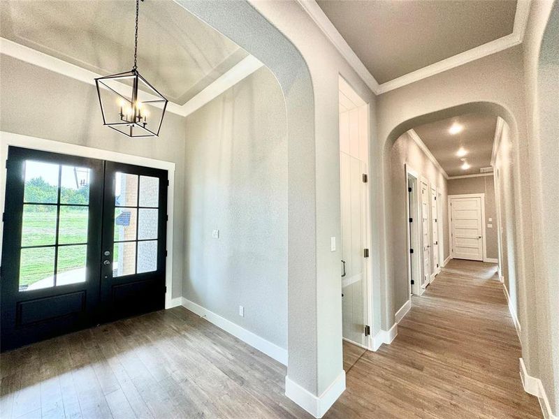 Entryway with french doors, crown molding, arched walkways, wood finished floors, and a chandelier