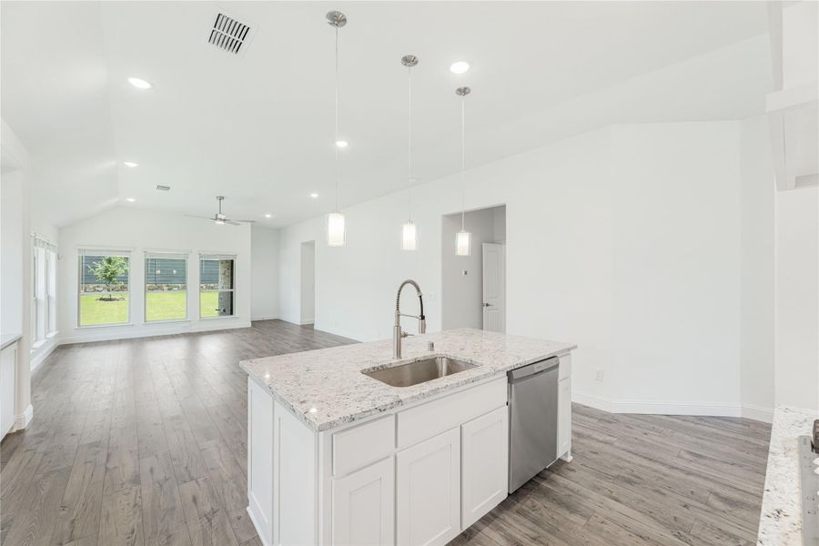 Kitchen island with granite countertop, sink, and white cabinets open to living area with vaulted ceiling and hardwood floors Kitchen island with granite countertop, sink, and white cabinets open to living area with vaulted ceiling and hardwood floors