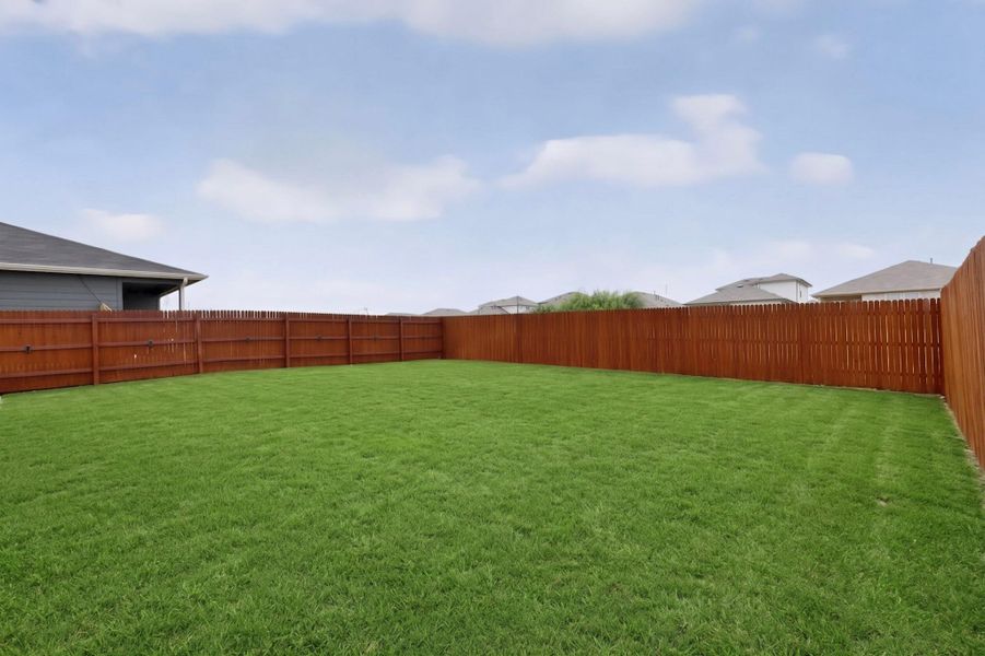 An expansive grassy lawn is fully enclosed by a tall wooden privacy fence.